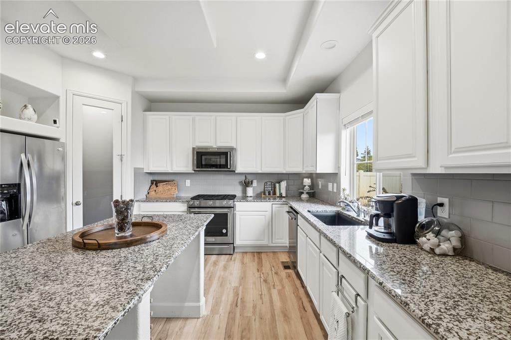 Image 9 of 50: Modern kitchen featuring light LVP plank flooring, white cabinetry, granite