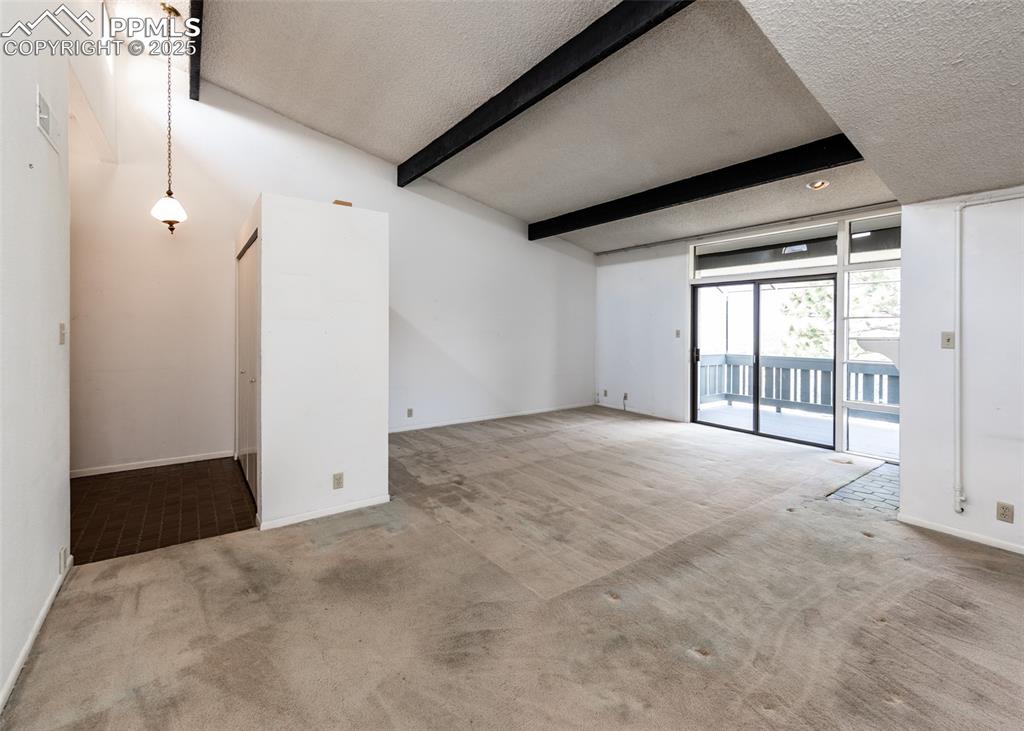 Image 12 of 40: Empty room featuring a textured ceiling, beamed ceiling, and carpet floorin