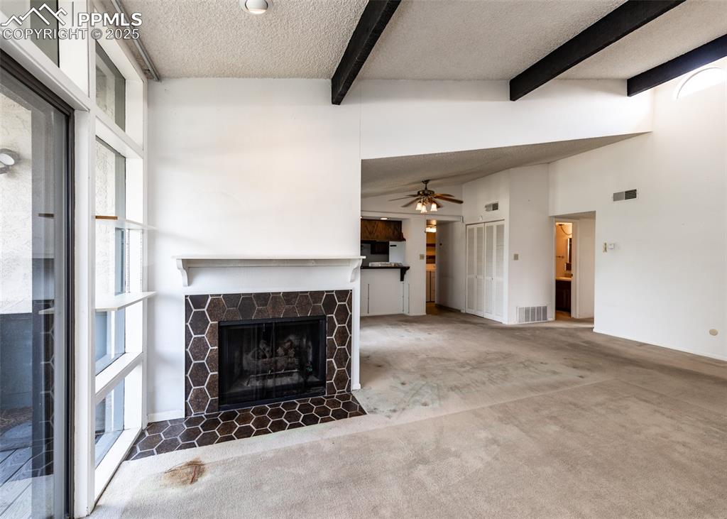 Image 15 of 40: Unfurnished living room with beam ceiling, a textured ceiling, a stone fire
