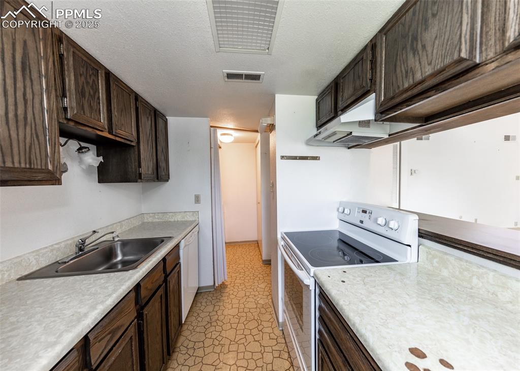 Image 16 of 40: Kitchen featuring white appliances, dark brown cabinetry, light countertops
