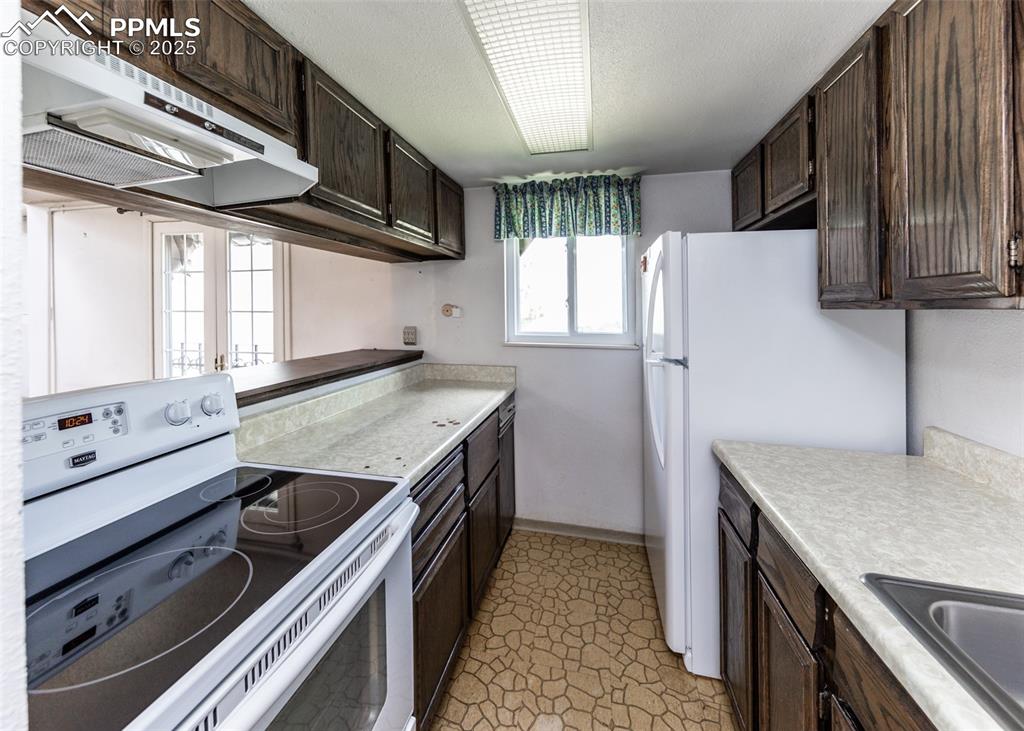 Image 18 of 40: Kitchen with white appliances, under cabinet range hood, dark brown cabinet