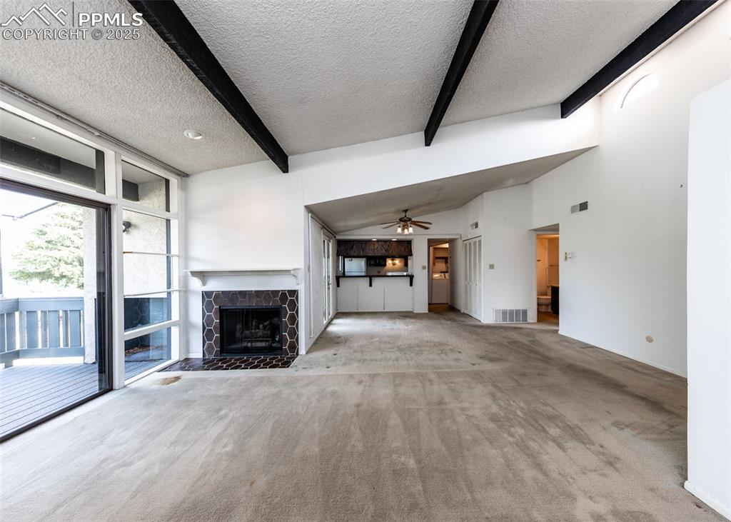 Image 6 of 40: Unfurnished living room with a textured ceiling, carpet floors, beamed ceil