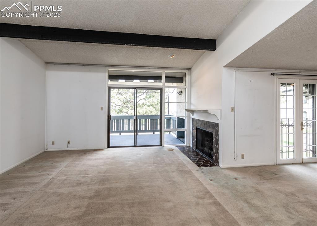 Image 9 of 40: Unfurnished living room with carpet flooring, beamed ceiling, a tiled firep