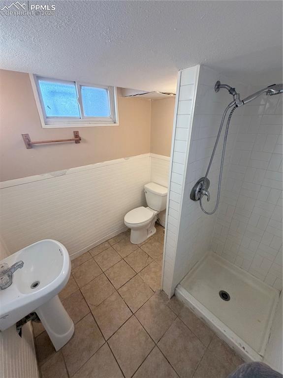 Image 11 of 15: Full bathroom with wainscoting, a stall shower, a textured ceiling, and lig
