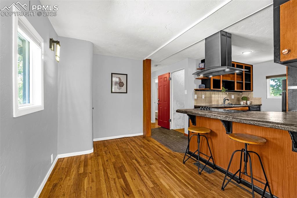 Image 12 of 42: Kitchen featuring island range hood, wood finished floors, dark countertops