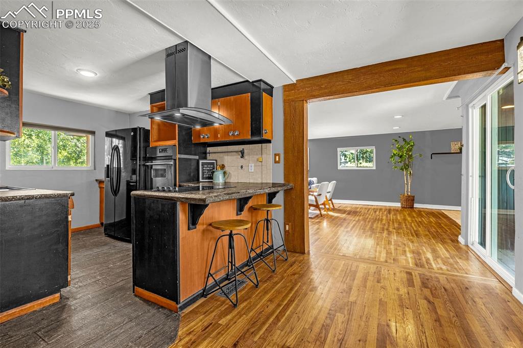 Image 13 of 42: Kitchen with island exhaust hood, black appliances, hardwood / wood-style f
