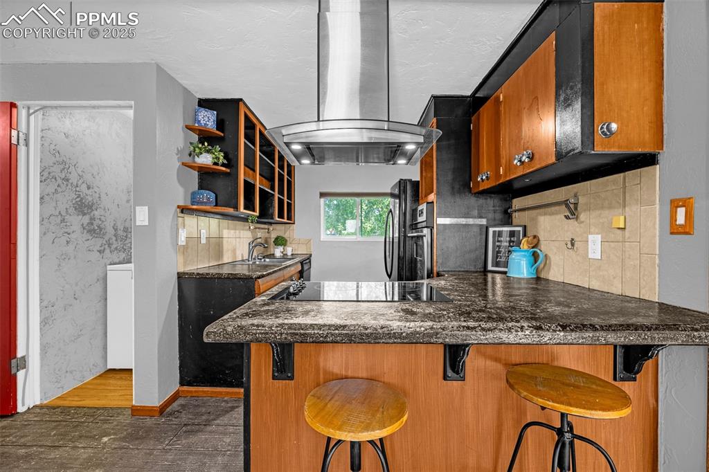 Image 15 of 42: Kitchen featuring wall chimney exhaust hood, black electric cooktop, dark w