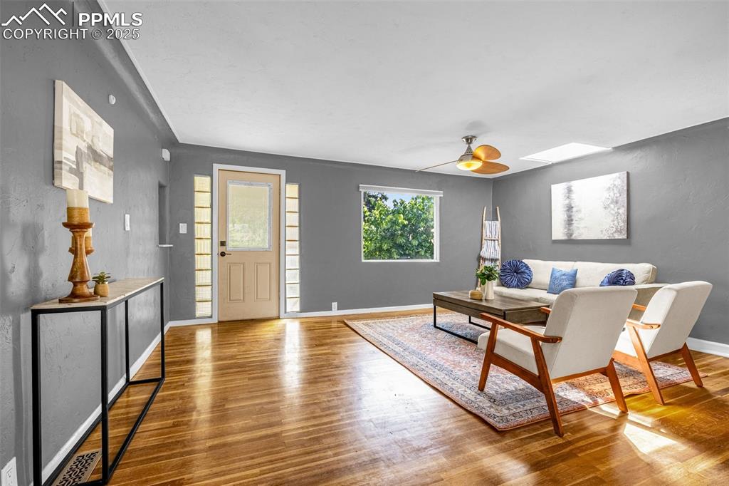Image 7 of 42: Living room with wood finished floors, a skylight, and a ceiling fan