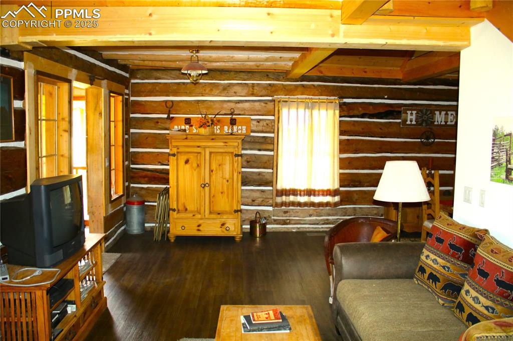 Image 17 of 28: Living room featuring dark wood-type flooring, rustic walls, and beamed cei