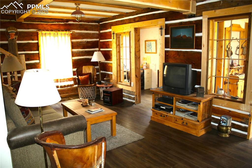 Image 18 of 28: Living room featuring wood walls, wood finished floors, and beamed ceiling