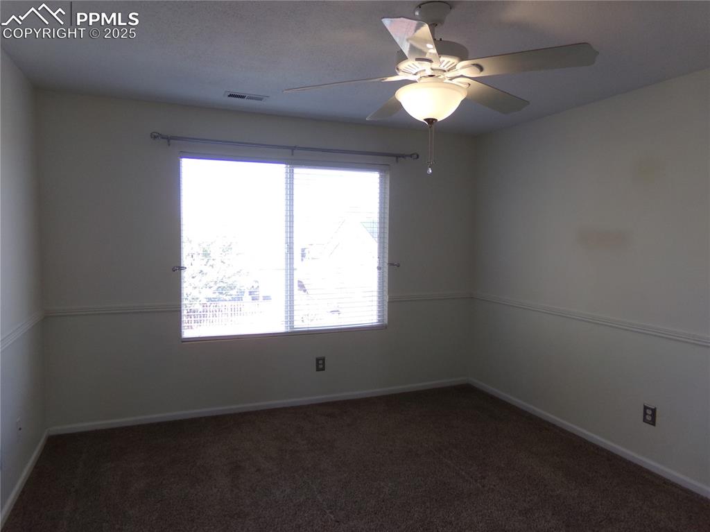 Image 15 of 29: Empty room featuring dark colored carpet and a ceiling fan