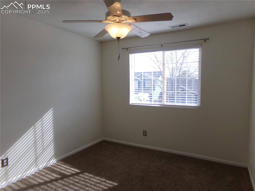 Image 21 of 29: Empty room with dark colored carpet and ceiling fan