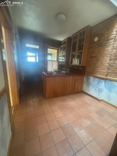 Image 21 of 50: Kitchen featuring dark countertops, a peninsula, brown cabinetry, and glass