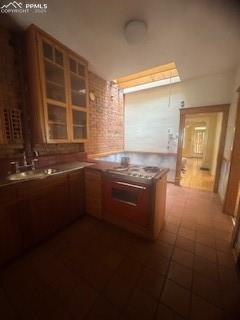 Image 22 of 50: Kitchen with brick wall, a peninsula, brown cabinetry, and light countertop