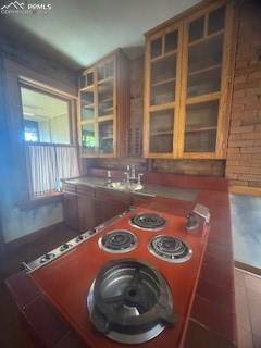 Image 23 of 50: Kitchen featuring brown cabinets, brick wall, and glass insert cabinets
