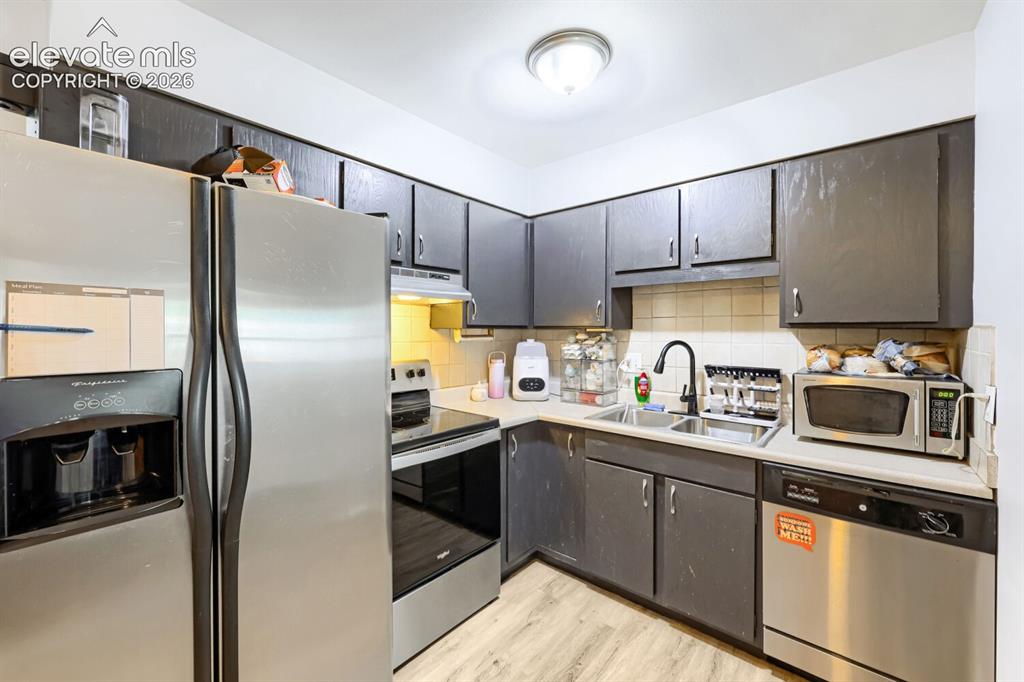 Image 7 of 26: Kitchen featuring stainless steel appliances, dark cabinetry, light-toned c