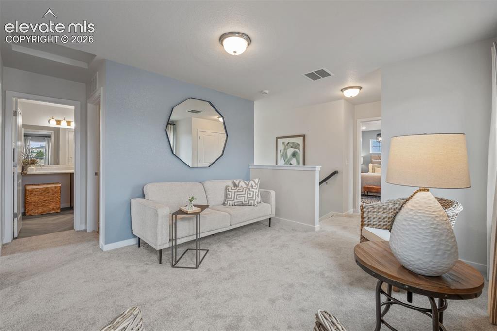 Image 15 of 26: Carpeted upper-level landing with a partial wall and stairway railing