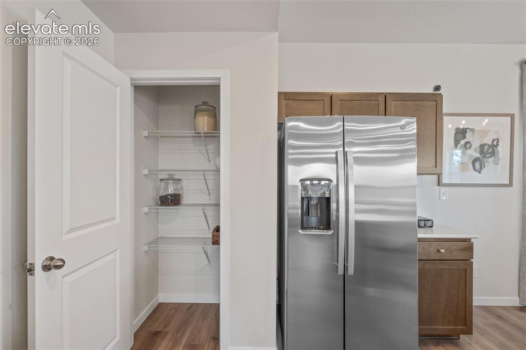 Image 8 of 26: Stainless steel side-by-side refrigerator, wood-finish flooring, and pantry