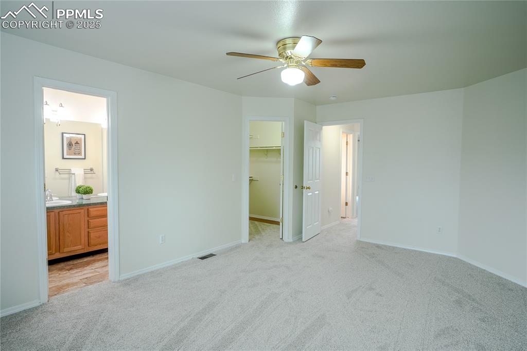 Image 13 of 37: Primary bedroom featuring a spacious closet, light carpet, ceiling fan, and