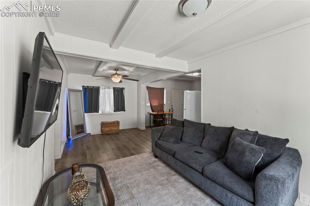 Image 10 of 19: Living area with a textured ceiling, a ceiling fan, beam ceiling, wood fini