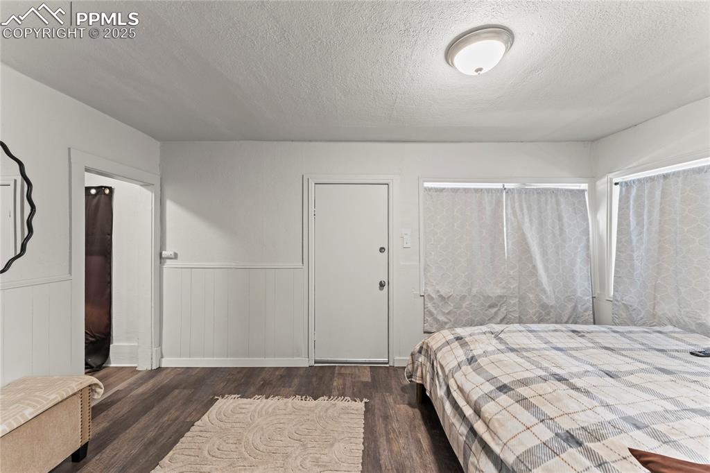 Image 12 of 19: Bedroom with wainscoting, a textured ceiling, and dark wood finished floors