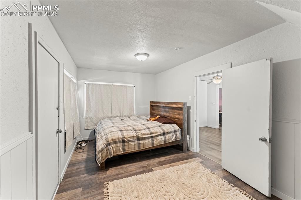 Image 13 of 19: Bedroom featuring a textured ceiling, wainscoting, and wood finished floors