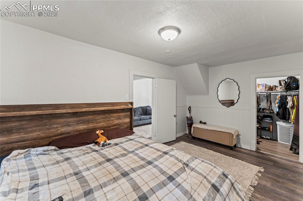 Image 14 of 19: Bedroom with a textured ceiling, wood finished floors, wainscoting, and a s