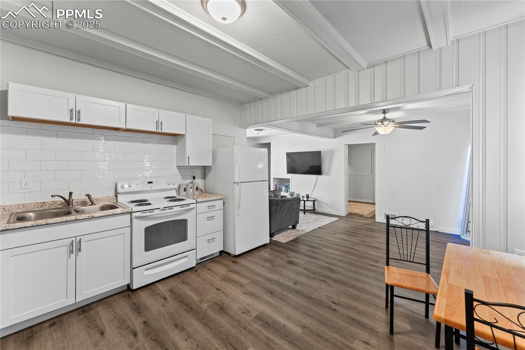 Image 5 of 19: Kitchen with white appliances, beamed ceiling, tasteful backsplash, white c