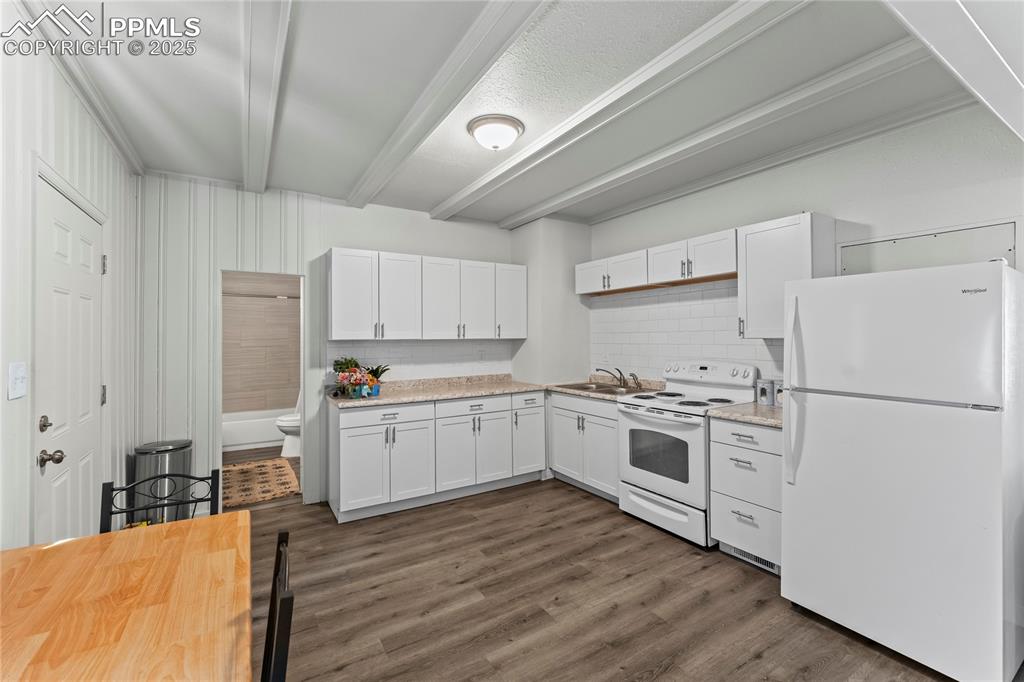 Image 6 of 19: Kitchen featuring white appliances, beamed ceiling, decorative backsplash, 