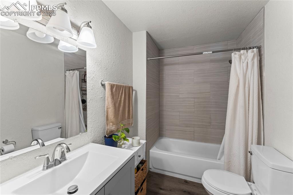 Image 7 of 19: Bathroom featuring a textured wall, vanity, shower / tub combo with curtain