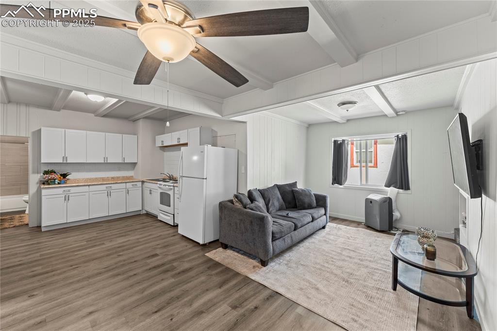 Image 9 of 19: Living room with beamed ceiling, wood finished floors, and a ceiling fan