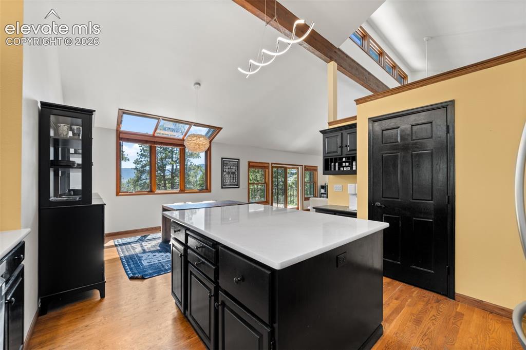 Image 15 of 47: Kitchen featuring a large central island with a white countertop and dark c