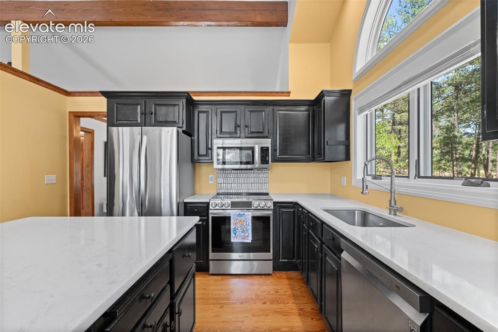 Image 16 of 47: Kitchen featuring dark cabinetry, stainless steel appliances, and light cou