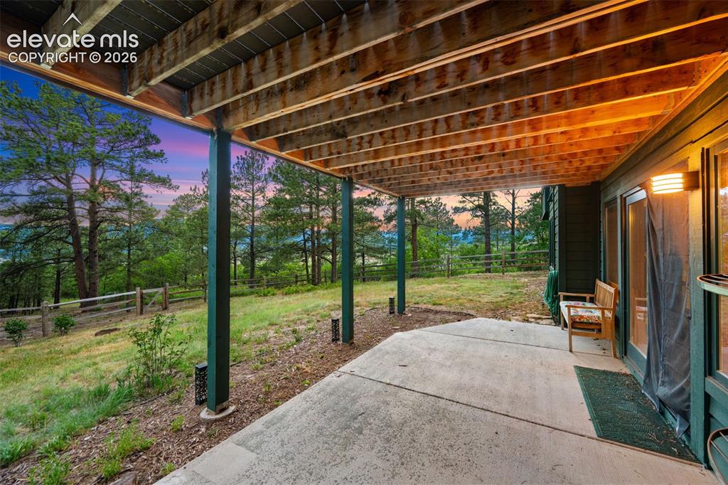Image 39 of 47: Covered concrete patio with exposed wood ceiling beams and a natural wood f