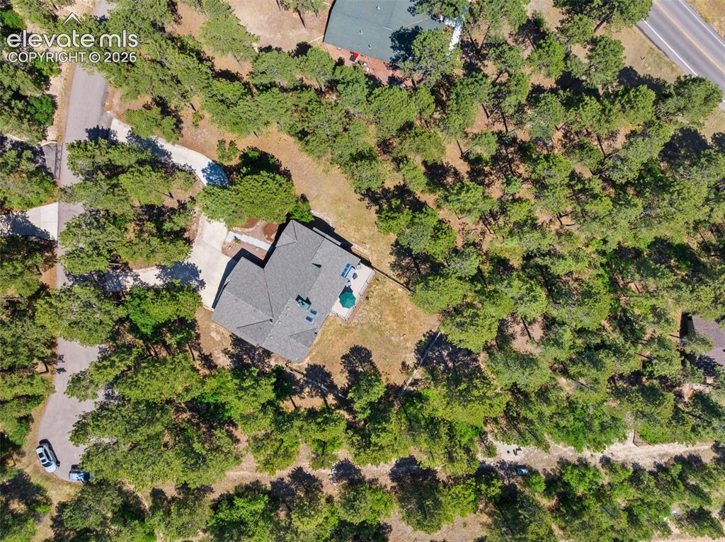 Image 46 of 47: Single-story residence set on a treed lot, featuring a grey shingle roof an