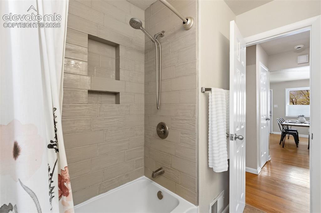 Image 21 of 47: Bathtub with subway tile surround, recessed shelving, and a brushed nickel