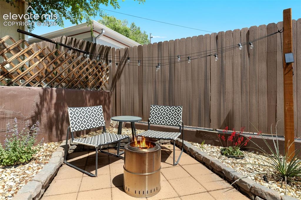 Image 38 of 47: Paved patio area featuring string lighting, wood fencing, a decorative latt