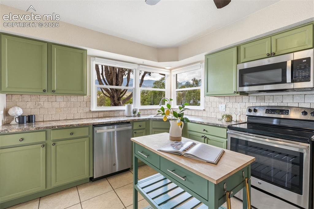Image 7 of 48: Kitchen featuring green cabinetry, stainless steel appliances, a tile backs