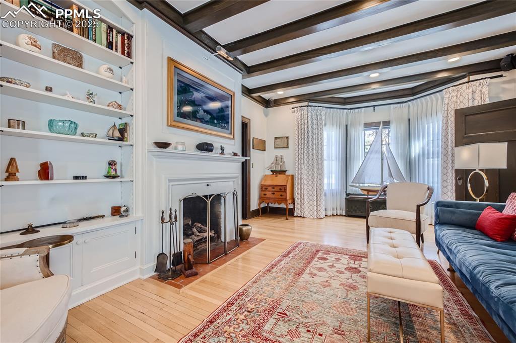 Image 19 of 49: Living room with beamed ceiling and light hardwood floors
