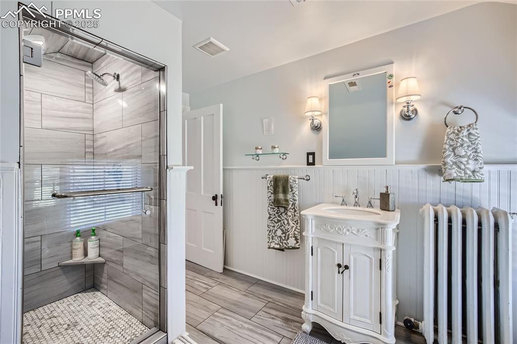 Image 44 of 49: Bathroom with tile floors, vanity, radiator heating unit, and a shower with