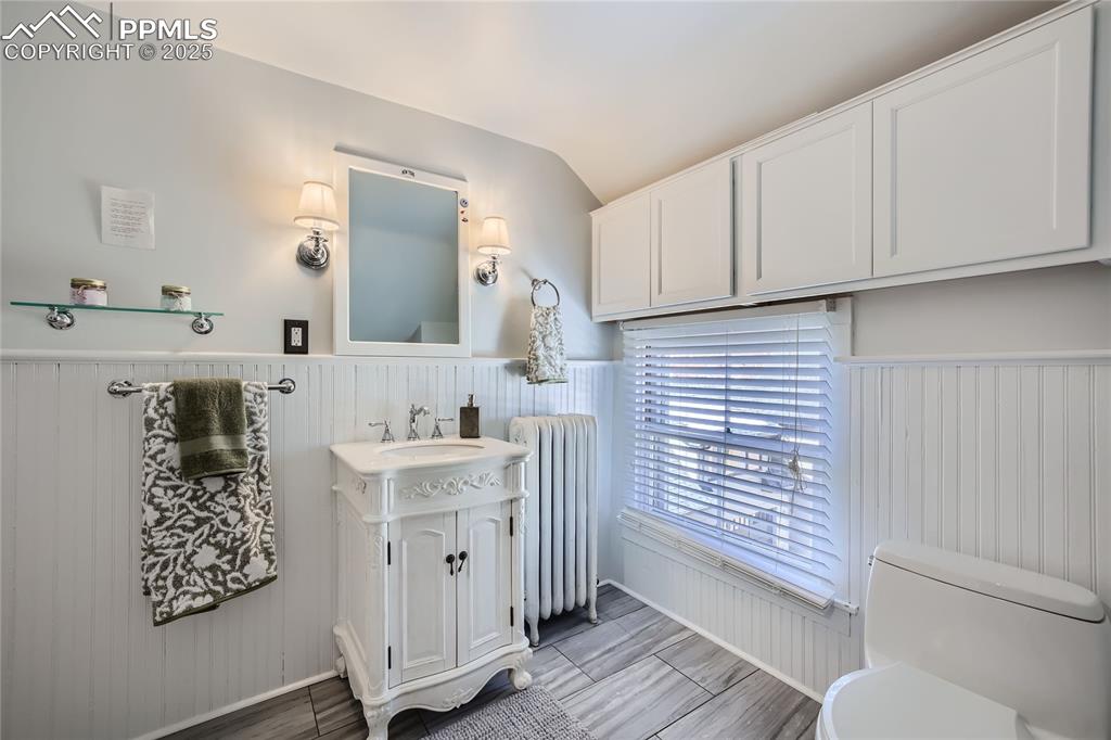 Image 45 of 49: Bathroom with vanity, tile flooring, toilet, vaulted ceiling, and radiator 
