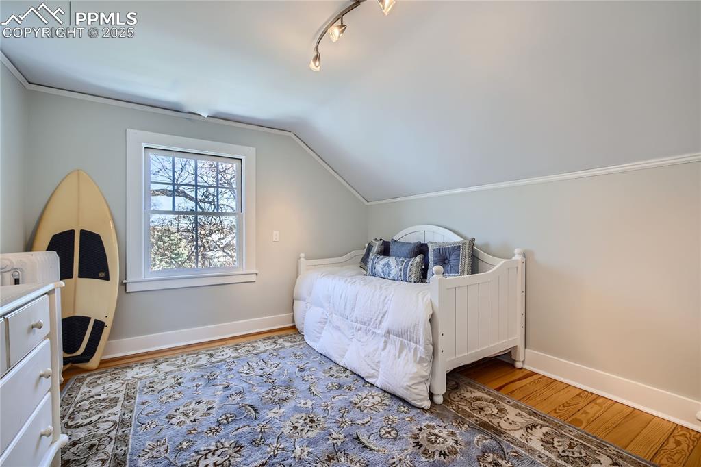 Image 46 of 49: Bedroom with lofted ceiling, track lighting, and light wood flooring
