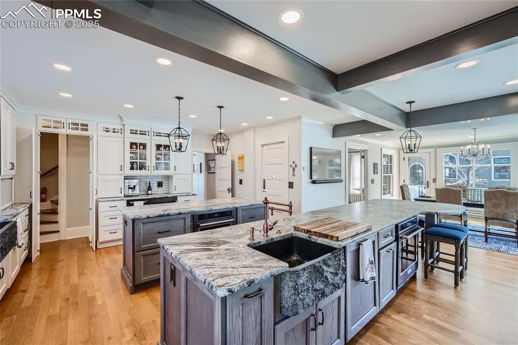 Image 9 of 49: Kitchen featuring light wood flooring, white cabinets, an island with sink,