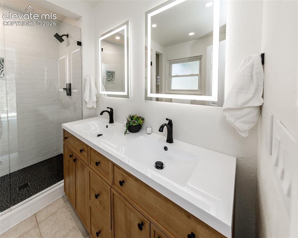 Image 14 of 30: Dual vanity with white integrated sinks, light wood-finish cabinetry, and m
