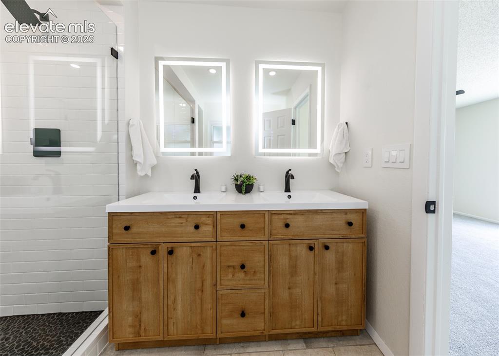 Image 15 of 30: Dual vanity with light wood-finish cabinetry, white countertop, and matte b