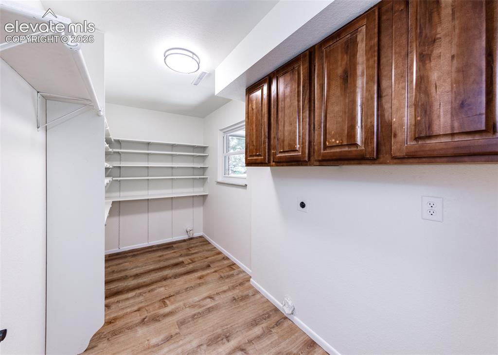 Image 23 of 30: Utility room featuring extensive built-in shelving, wood-finish flooring, a