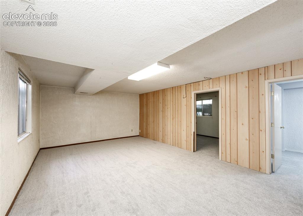 Image 24 of 30: Spacious room featuring light-toned carpeting, wood paneling, and a window