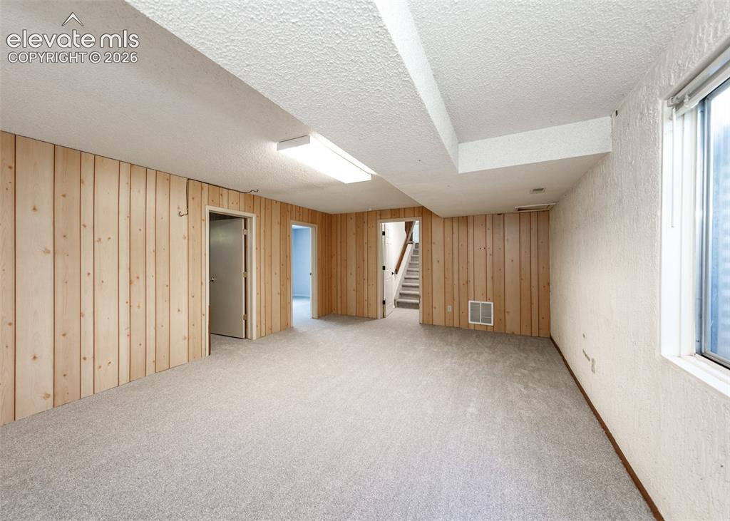 Image 25 of 30: Spacious finished room featuring light wood paneling, textured white walls,