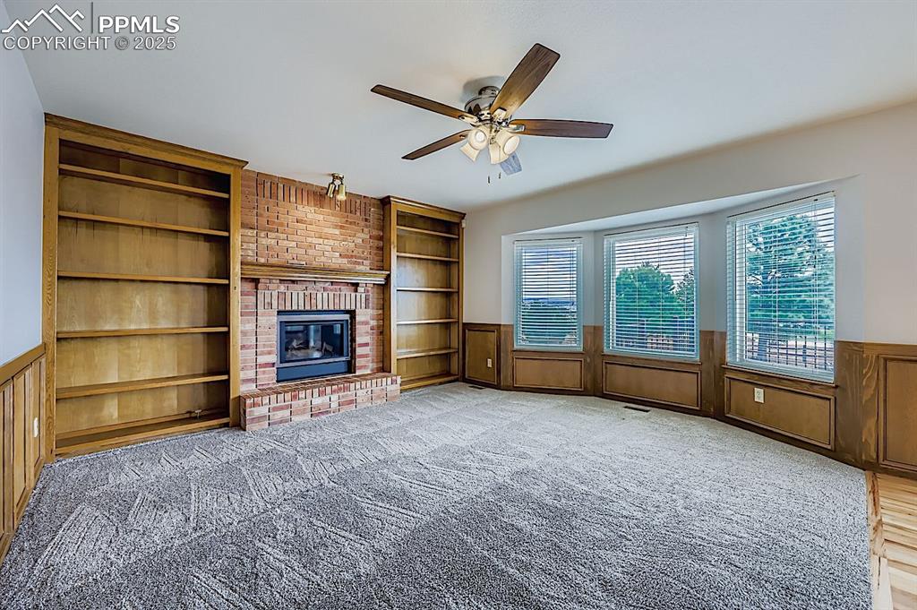 Image 16 of 48: Unfurnished living room with built in features, wainscoting, ceiling fan, l