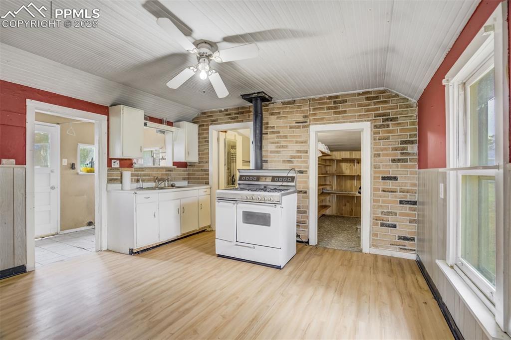 Image 33 of 50: Kitchen with a wood stove, white gas stove, brick wall, white cabinetry, an